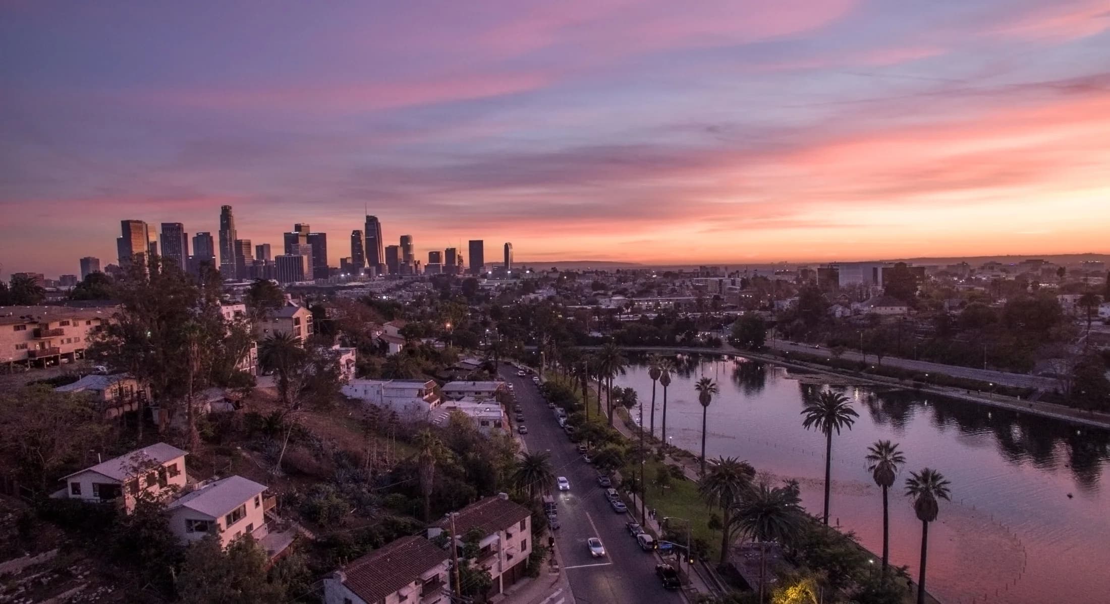 Echo Park Lake and palm-lined neighborhood streets under a pink sunset, with Downtown Los Angeles beyond.