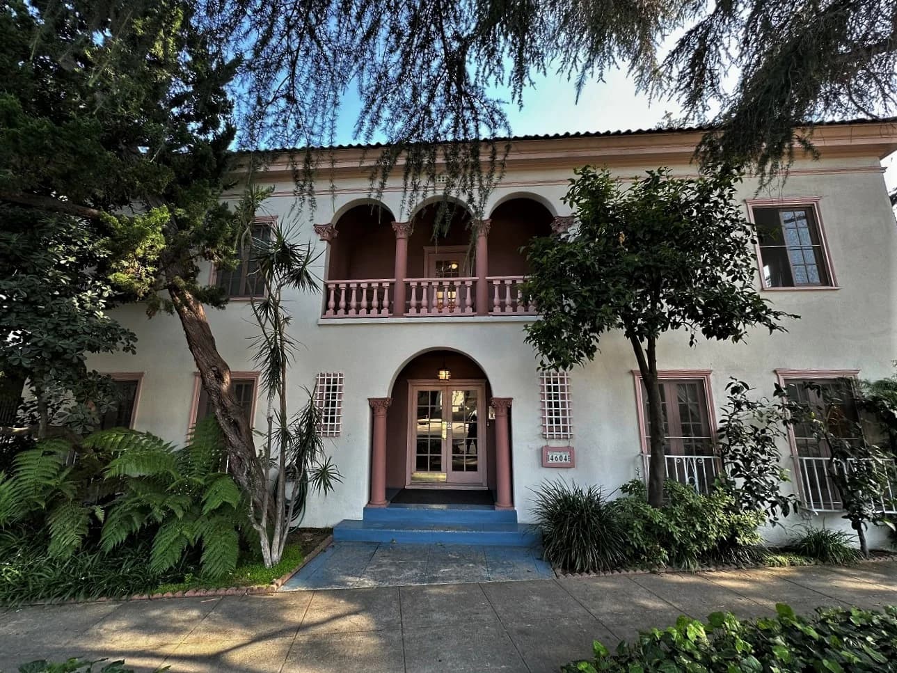 A stucco apartment facade with arched balconies, pink columns and leafy landscaping at 4604 Los Feliz Boulevard.