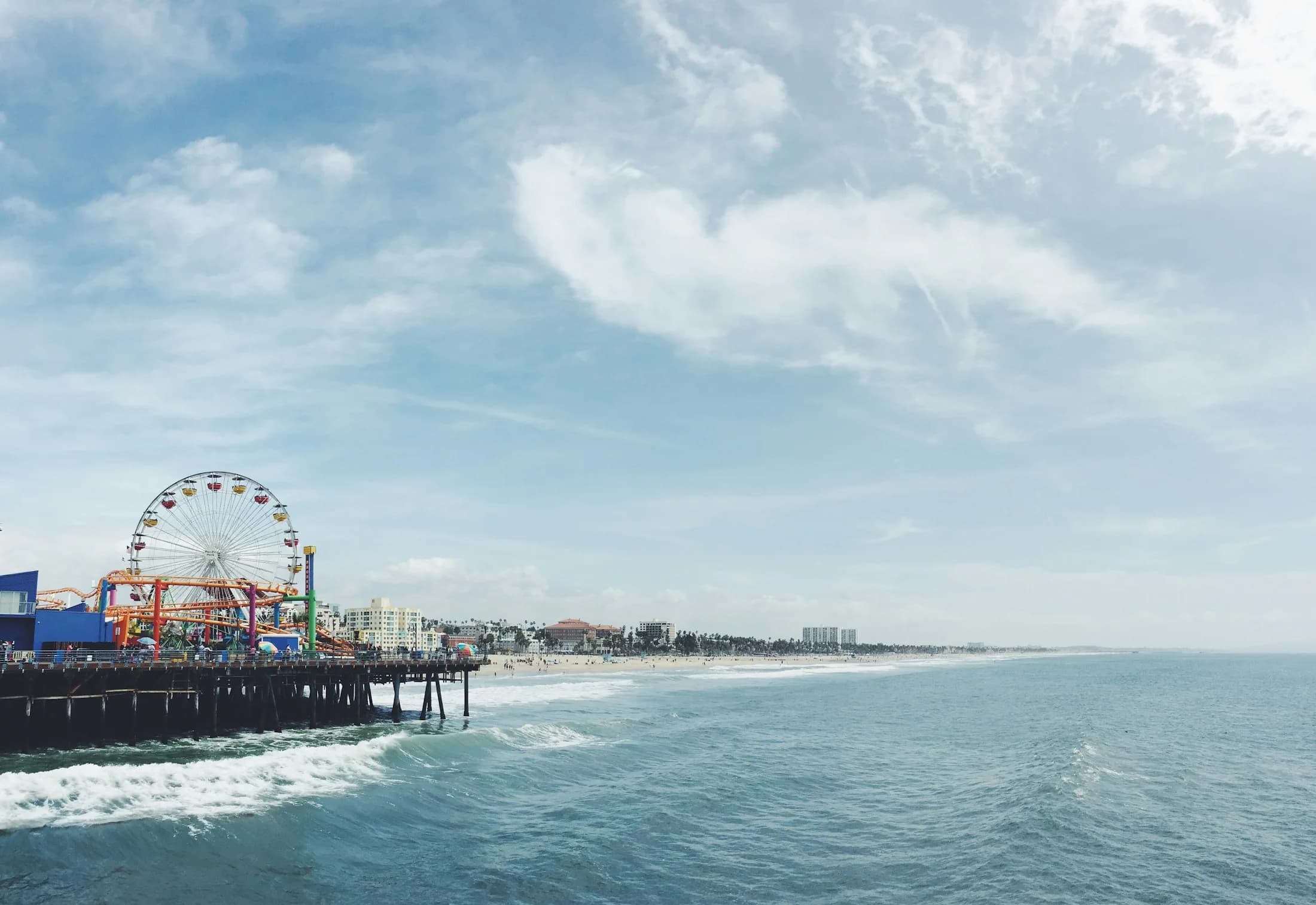 Santa Monica Pier, its Ferris wheel, and the coastline beneath a cloudy sky.